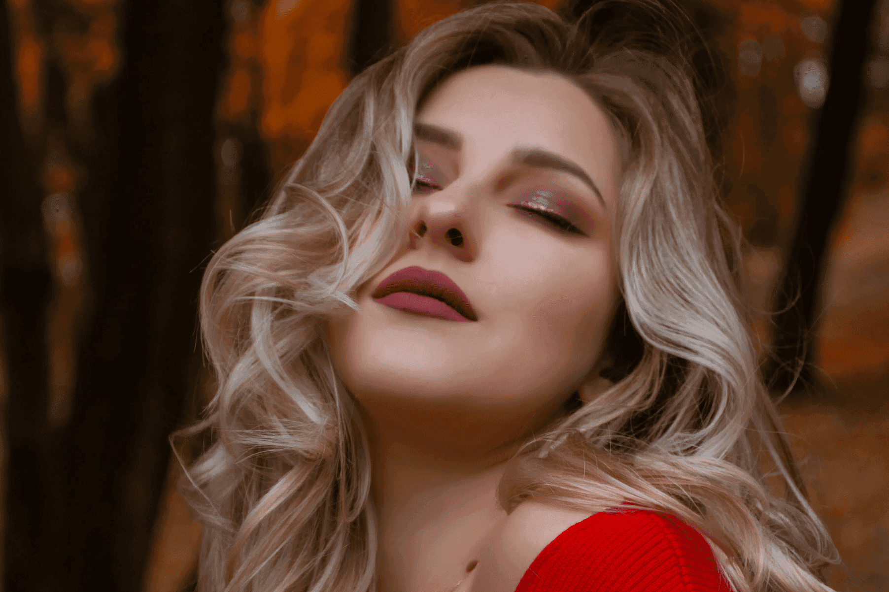 Woman in a red sweater with closed eyes, enjoying the autumn forest scenery.