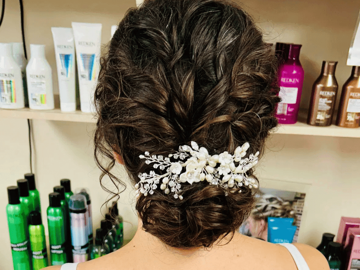 Braided updo with floral hair accessory in a salon setting, surrounded by hair products.