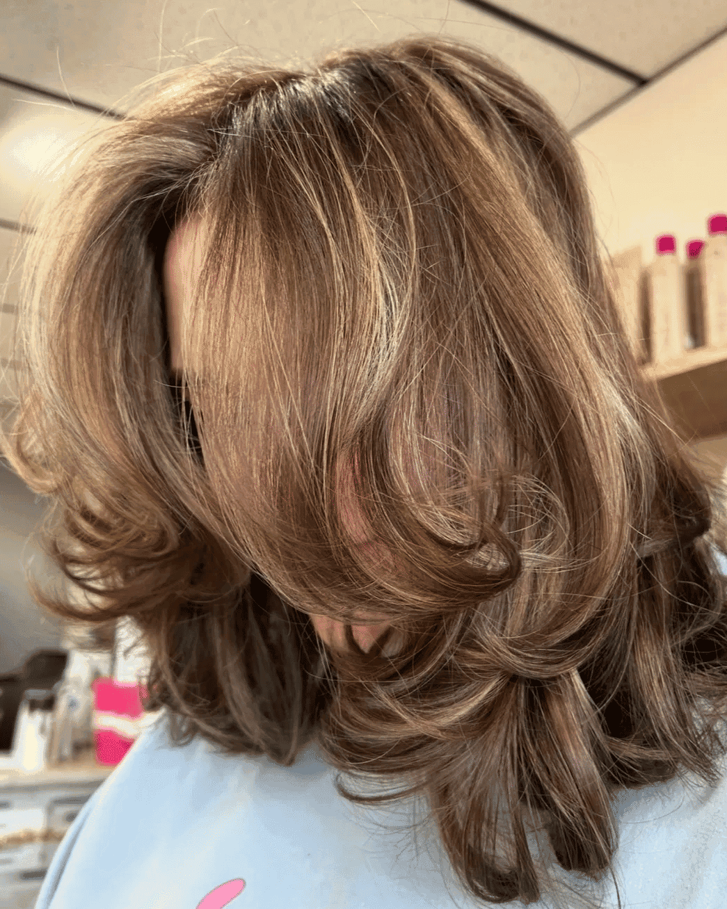 Elegant layered hairstyle with soft waves and highlights in a salon setting.