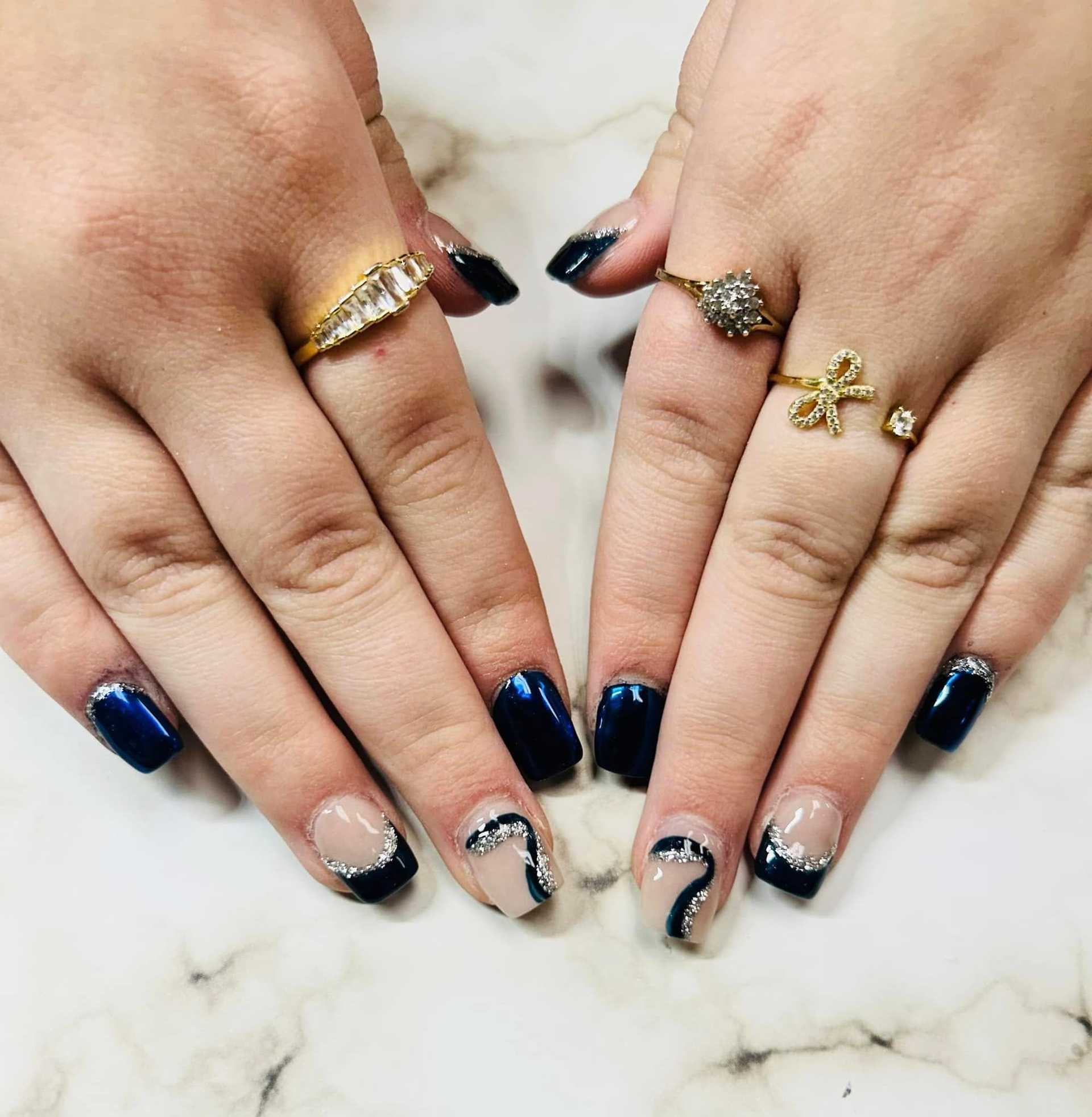 Elegant navy and silver nail art on manicured hands with stylish rings.