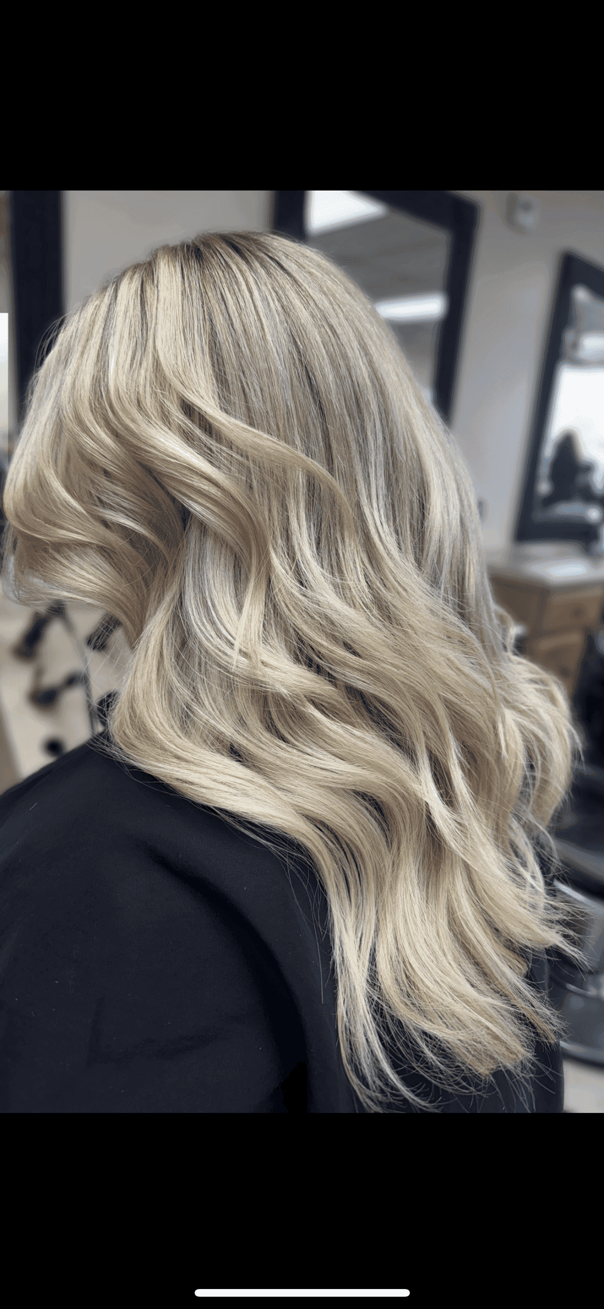 Blonde wavy hairstyle cascading over shoulders in a salon.